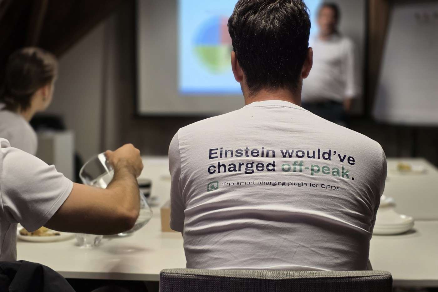 Teamleden in Scopt-T-shirts met de zin "Einstein would've charged off-peak." tijdens een presentatie